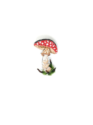 A hand-embroidered brooch that looks like a red spotted mushroom.