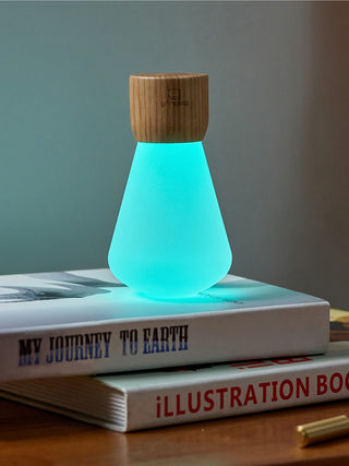 An upside down light bulb with a wooden base, illuminated in light blue, on top of books.