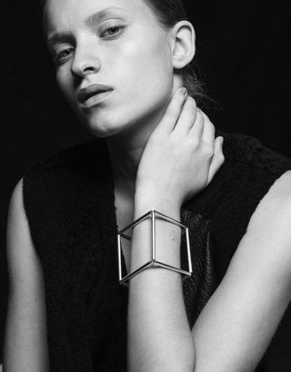 A black and white picture of a model wearing A gold geometic bracelet in the form of a cube.