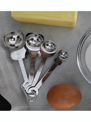 Stainless steel measuring spoons in the shape of guitars next to a stick of butter and an egg.