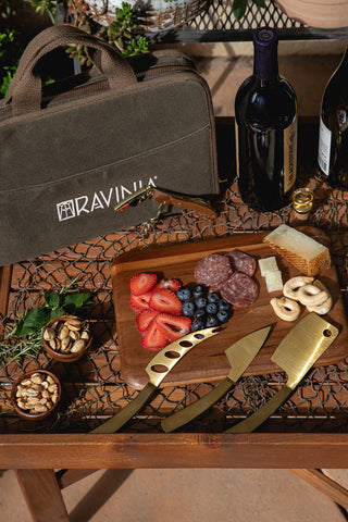 A wooden table with a loaded charcuterie board, the travel cheese knife set and its case, and two bottles of wine.