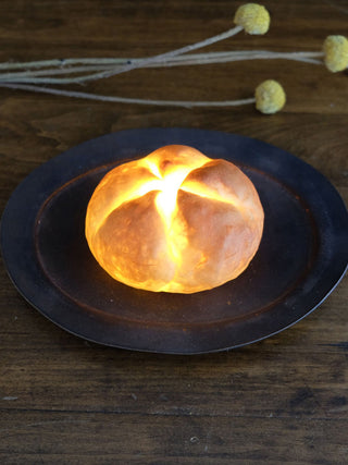 The Kaiser Roll Real Bread Lamp sitting on a plate looks like the real thing, thanks to the warm, amber glow from its LED.