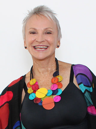 A smiling model in a black top wearing a Three strands of beads made from both resin and wood in a bright mix of colors are hung from a lobster-claw clasp.