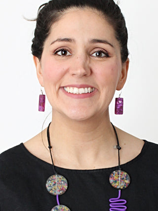 On a smiling model in a black top, Earrings made of rectangular purple resin bead dangle from a two inch French wire.