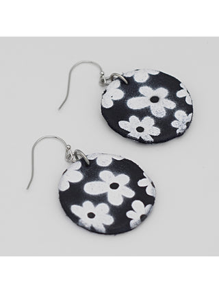 Angled view of Circular black earrings with a white flower print, with a French wire above.