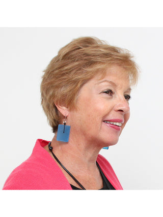 A smiling woman wearing A pair of translucent blue, rectangular earrings with silver-toned hooks.
