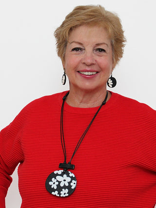 A smiling model in a red top wearing A playful flower design in black and white, on a leather cord.