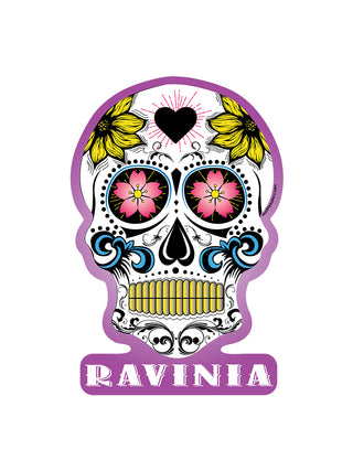 A sugar skull with yellow and pink flowers, blue embellishments, and a pink border with "Ravinia" under it.