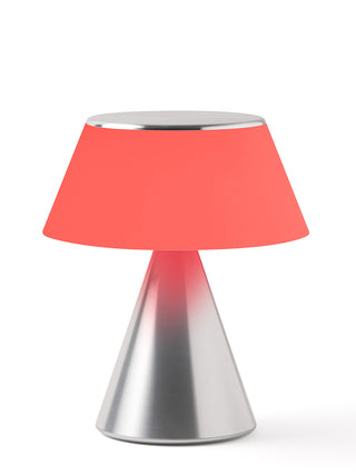 A lamp with a triangular aluminum base and an illuminated  red shade.