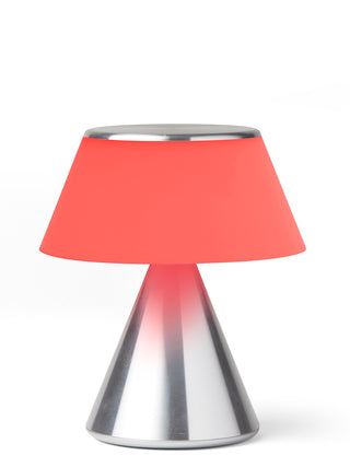 A lamp with a triangular aluminum base and an illuminated red shade.