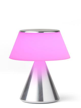 A lamp with a triangular aluminum base and an illuminated  fuchsia  shade.
