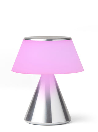 A lamp with a triangular aluminum base and an illuminated  pink shade.