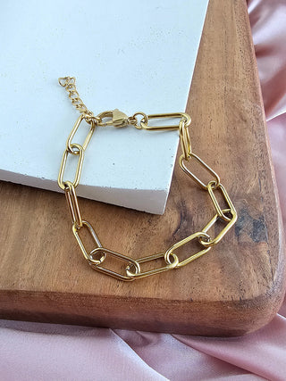 A gold chain link bracelet with a hook clasp, laying on a wooden plate.