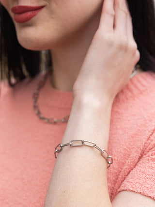 A close-up image of a model in a pink shirt wearing the silver Luxe chunky paper clip bracelet.