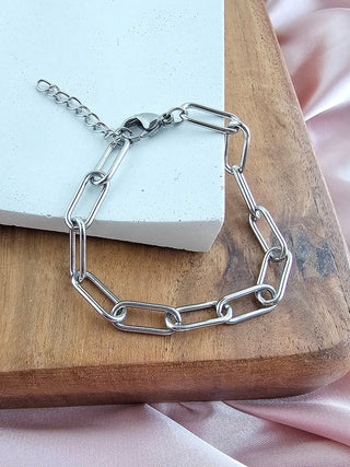 A silver chain link bracelet with a hook clasp, laying on a wooden plate.