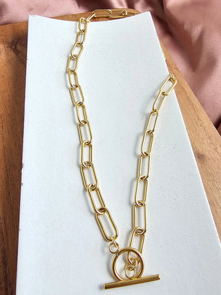A gold chain link necklace with a toggle clasp, laying on a white plate.