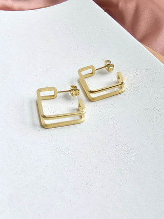A pair of gold geometric hoop earrings laying on a white plate.