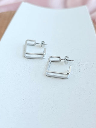A pair of silver geometric hoop earrings laying on a white plate.