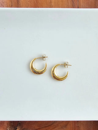 A pair of gold moon-shaped open hoop earrings on a white background.