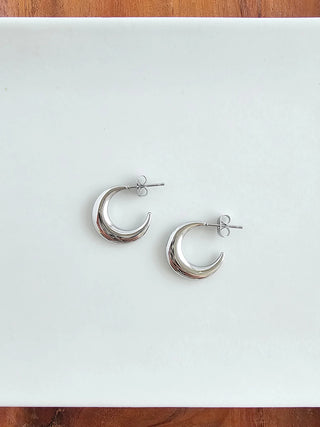 A pair of silver moon-shaped open hoop earrings on a white background.