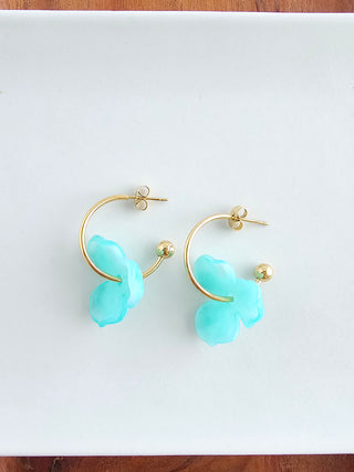 A pair of gold hoop earrings with an aqua resin flower on each.
