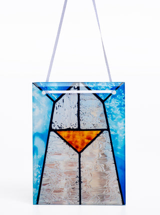 A rectangular stained glass ornament with blue, white and amber geometric shapes, hanging from a white ribbon.
