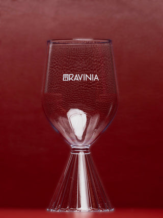 The clear Milan 12oz wine glass with the Ravinia name and logo in white displayed on a red background.