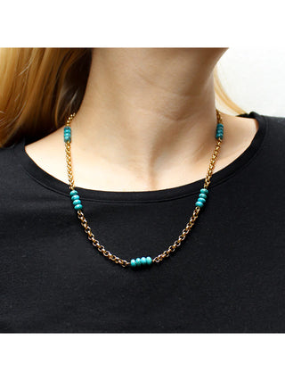 A brass link chain necklace interspersed with five turquoise bead stacks, on a model who is wearing a black top.
