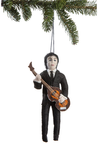 A felt ornament of a young Paul McCartney in a suit, playing a bass guitar, hanging from a holiday tree branch.