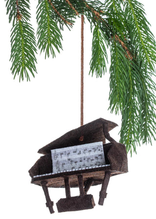 A felt ornament of a piano with sheet music, hanging from a Christmas tree branch.