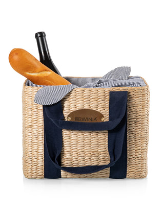 An open picnic basket tote, its blue straps down, a baguette and bottle of wine showing out the top.