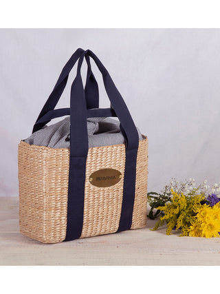 A woven picnic basket with blue straps that are also handles, with flowers adjacent.