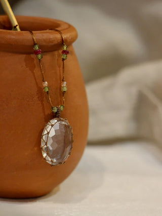 The necklace hung over the side of a small pot, with focus on the quartz crystal pendant.