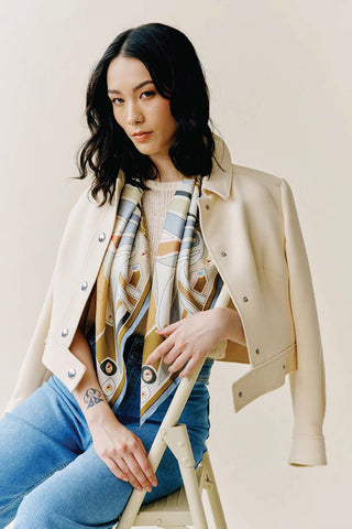 A woman sitting in a chair wearing a knotted scarf of blue, brown, and khaki visible under a white jacket.