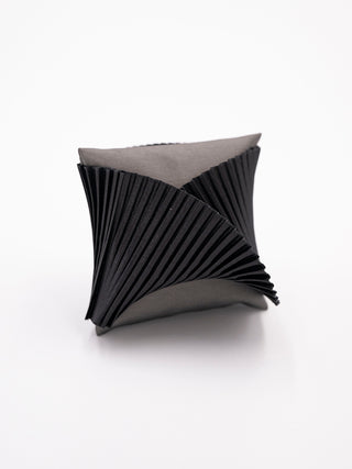 A black pleated silk cuff bracelet on a gray pillow.