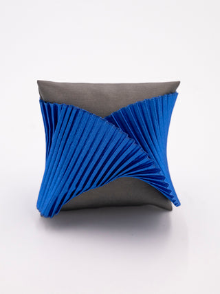 A blue pleated silk cuff bracelet on a gray pillow.