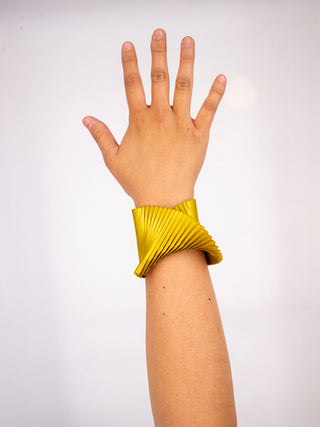 A gold pleated silk cuff bracelet on a wrist.