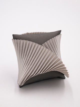 A silver pleated silk cuff bracelet on a gray pillow.