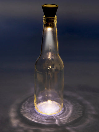 A solar light in the shape of a cork illuminating a bottle surrounded by darkness.