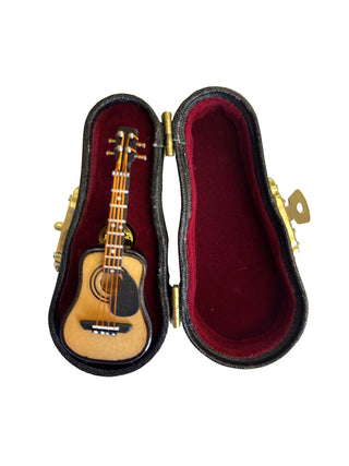 A lapel pin that looks like a steel string guitar in a red, velvet-lined case.