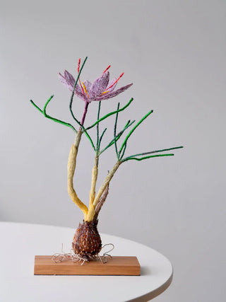 A hand-embroidered art piece that resembles a saffron crocus, sitting on a wooden base.