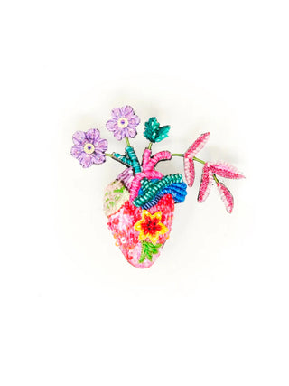 An embroidered brooch in the form of an anatomical heart with colorful flowers blooming from it.