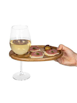 An oval wooden tray with a wine glass in its slot on the left, appetizers in the middle, and a hand holding it on the right.