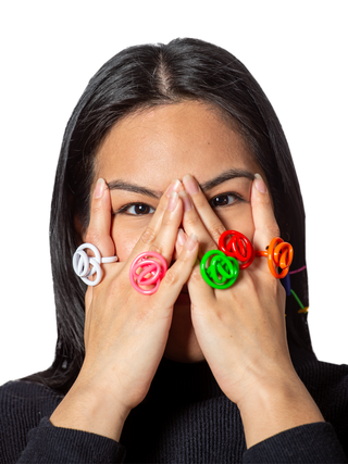 A woman partially covering her face with her hands, which are adorned with colorful squiggle plastic rings.
