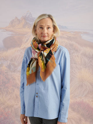 A woman in a blue shirt wearing a colorful embroidered wool scarf tied around her neck.