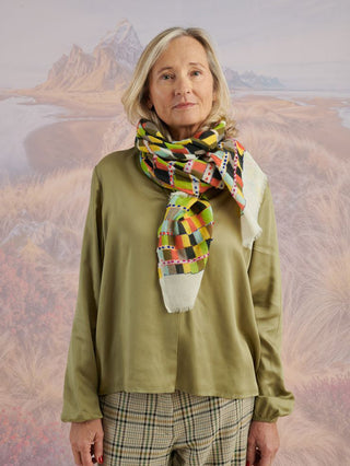 A woman with a green shirt wearing a colorful wool scarf with colorful embroidery.