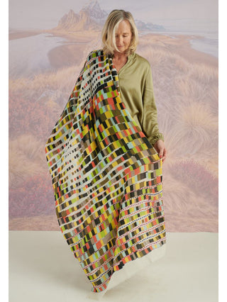 A woman holding a colorful scarf with colorful embroidery draped on her arm.