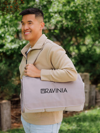A man holding the rolled pastel beige plaid blanket tote on his shoulder.