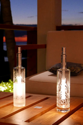 An outside dining area by the beach, with two bottlelight lamps in decorated glass bottles sitting on a wooden table.