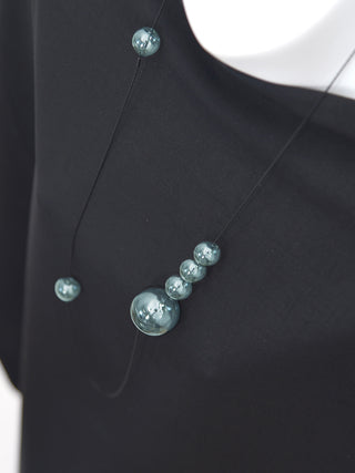 A mannequin wearing a black shirt and a long wire necklace with six glass orbs in various places.
